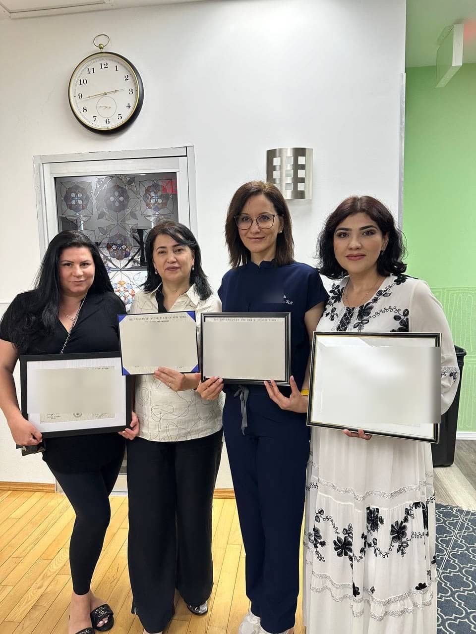 Four students in the classroom holding framed New York State Registered Professional Nurse certificates